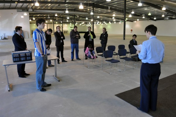 Candidates and others listen to the returning officer explain the ballot draw process.